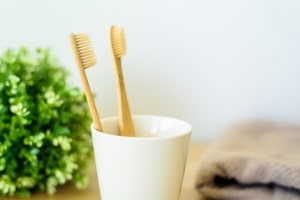 Two wooden toothbrushes in ceramic cup at bathroom.